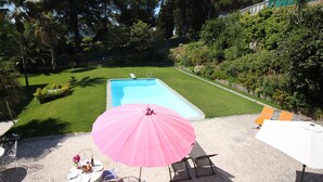 A backyard with a swimming pool, a pink umbrella, and outdoor seating. - Cascais Downtown, Villa With Pool and Garden (Cascais)
