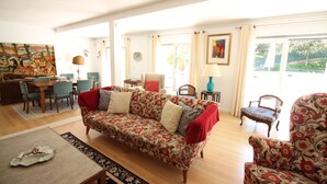 A living room with a patterned sofa, a dining area with chairs, a coffee table, and a painting on the wall. - Cascais Downtown, Villa With Pool and Garden (Cascais)
