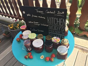 Ein Tisch mit Gläsern voll Marmelade und Erdbeeren, ein Schild, das eine Speisekarte für das Restaurant anzeigt, und ein Holzzaun im Hintergrund.