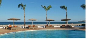 Ein Poolbereich mit Liegestühlen und Sonnenschirmen, mit freiem Blick auf das Meer und einem gepflegten Pool.