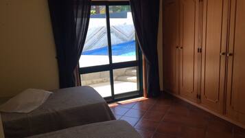 Una habitación con dos camas, una puerta corrediza de vidrio al exterior y armarios de madera.