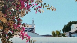 Une vue sur la piscine, avec une personne se relaxant sur une chaise longue, un ciel bleu dégagé et, au fond, un bâtiment dont le toit présente un motif particulier.