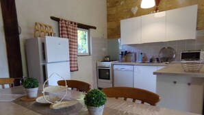 Een keuken met witte kasten, een fornuis en een vaatwasser. Er staan twee houten stoelen bij een tafel met placematen en potplanten.