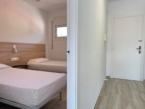 A hotel room with two beds, a window, a door, and a small table.