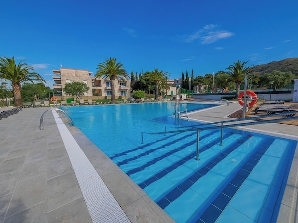 A swimming pool with clear blue water, surrounded by palm trees and a modern building in the background.