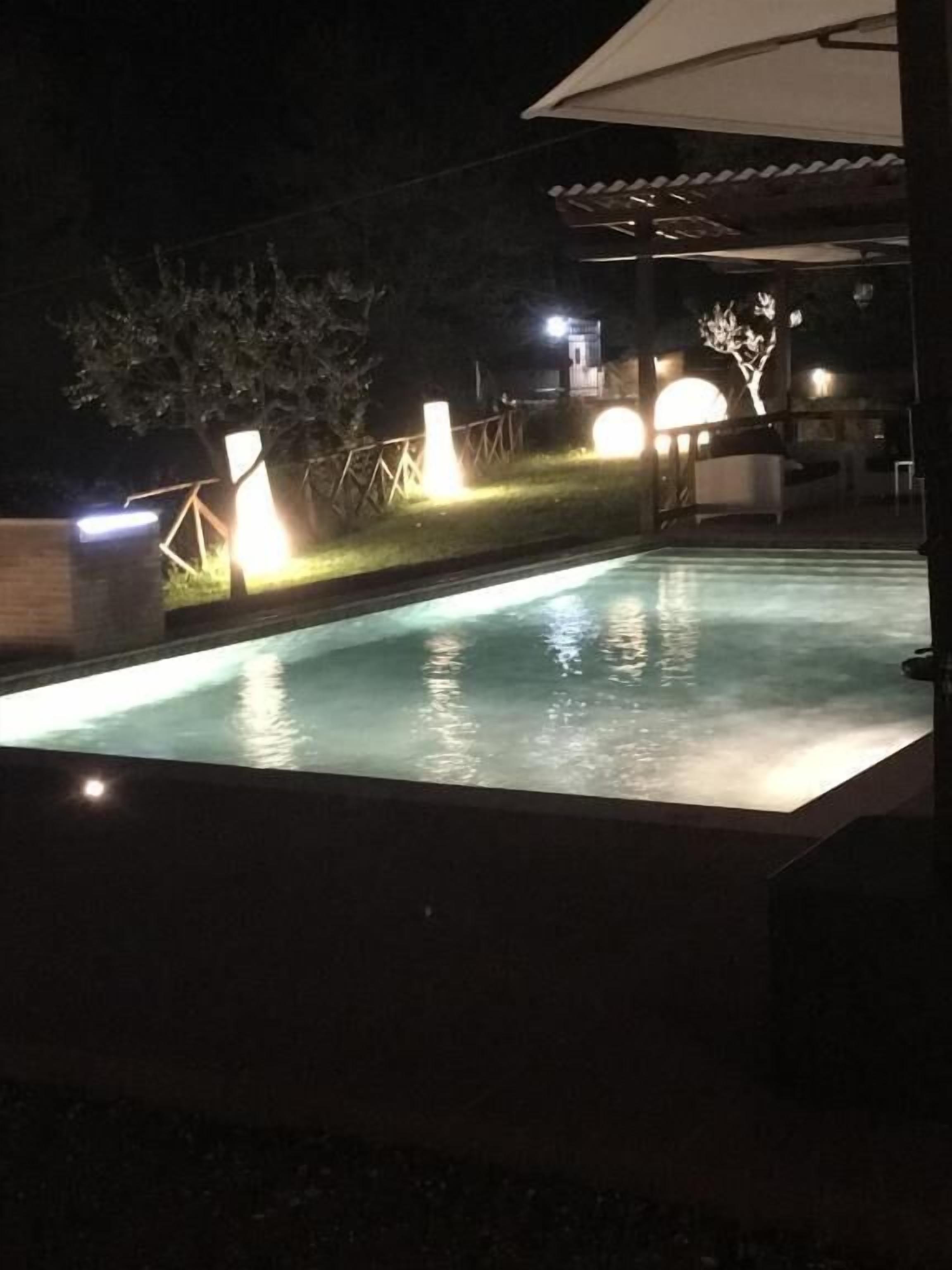 Piscina nocturna con luces circundantes y un área techada.