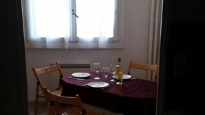 Un comedor con una mesa dispuesta para cuatro personas, incluyendo platos, vasos y una botella. Hay cuatro sillas de madera alrededor de la mesa.
