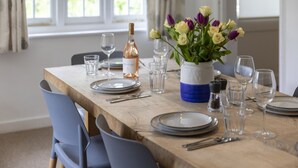A dining table set with plates, glasses, and a bottle of wine, with a vase of flowers in the center.