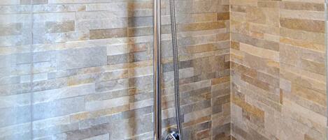 Dusche mit Regendusche und Handbrause, vor einer mit Steinmuster belegten Wand.