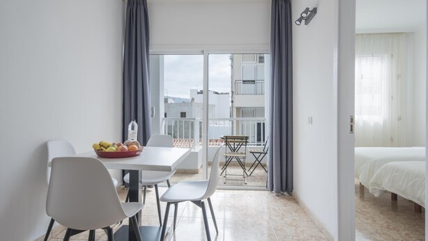 Une chambre d’hôtel compacte avec un balcon, un coin repas comprenant une table et des chaises, et un lit avec une literie blanche.