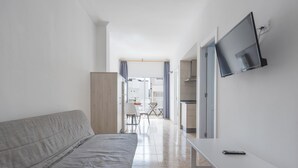 Une pièce moderne et minimaliste, avec un canapé gris, un téléviseur blanc fixé au mur et une petite table sur laquelle se trouve une télécommande.