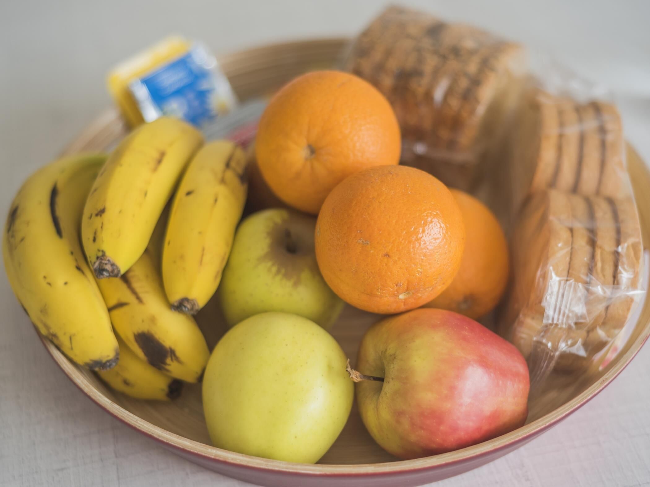 Un tazón con plátanos, manzanas, naranjas y pan.