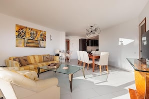 A modern living room with a sofa, a glass coffee table, and a dining area with chairs and a table.