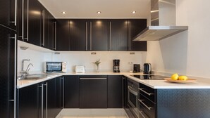 Uma cozinha moderna com armários pretos, eletrodomésticos de aço inoxidável e bancada branca.