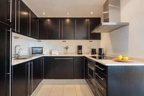 A modern kitchen with black cabinets, stainless steel appliances, and a white countertop.