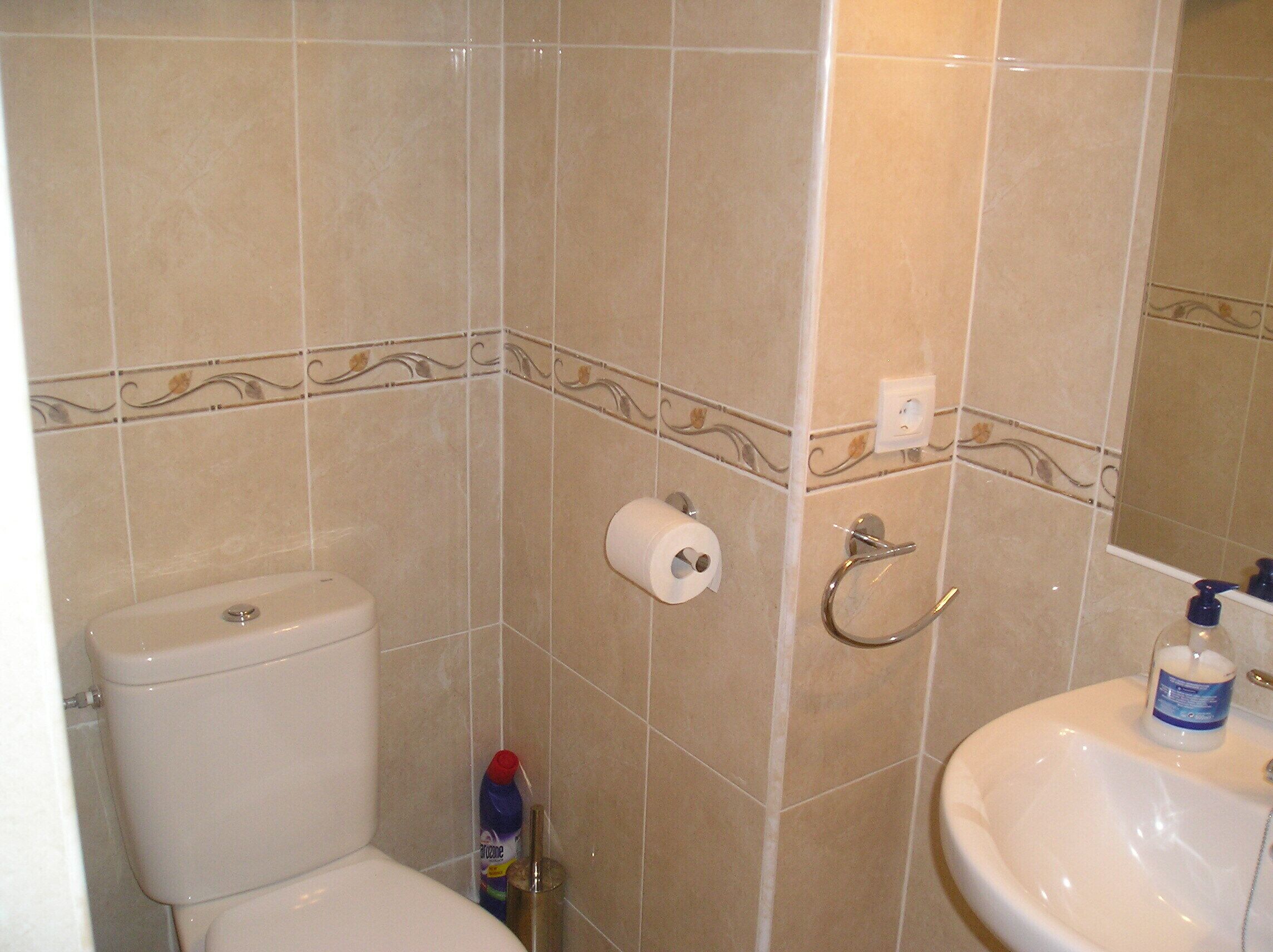 A bathroom with beige tiles, a toilet, a sink, and a bottle of hand soap.