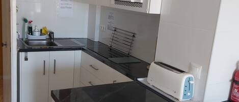 A compact kitchen with white cabinets, a black countertop, a microwave, and a toaster.