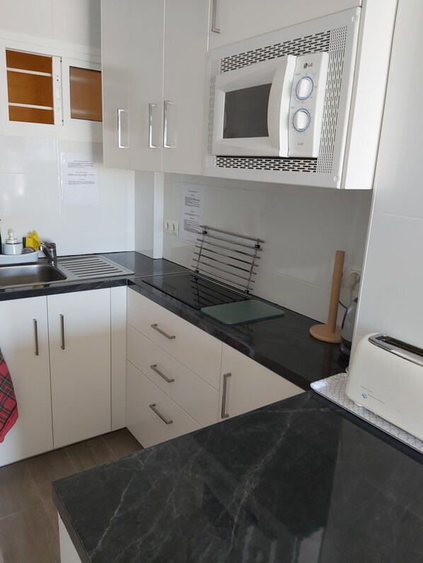 A modern kitchen with white cabinets, a black countertop, a microwave, a toaster, and a sink.