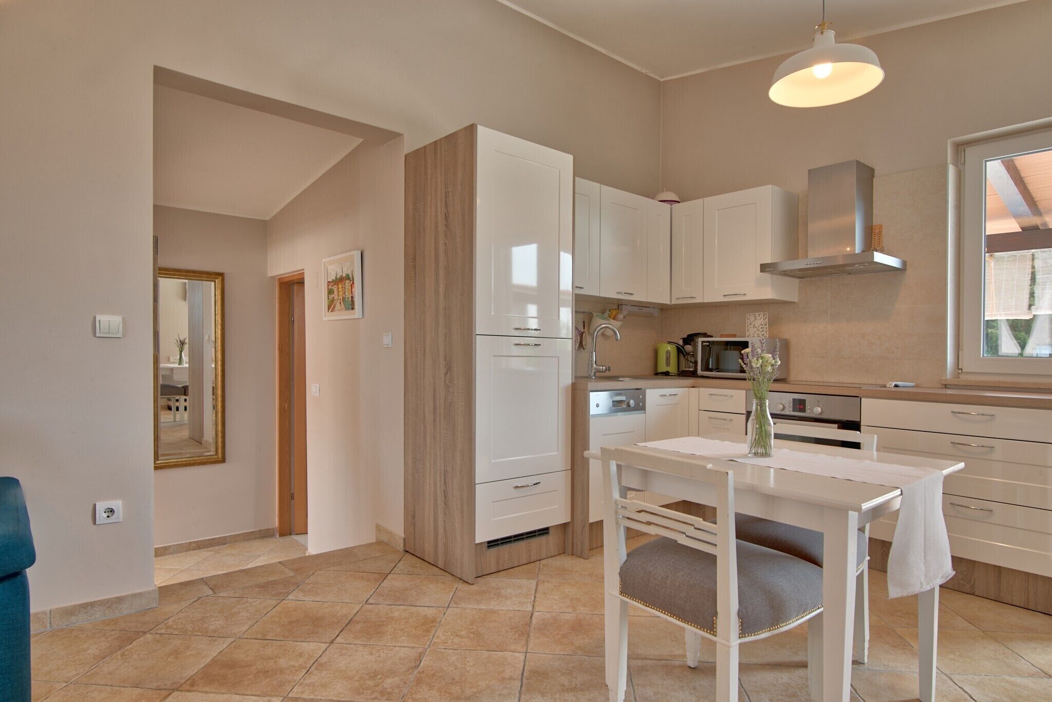 A modern kitchen with white cabinets, a dining table, and a hanging light fixture.