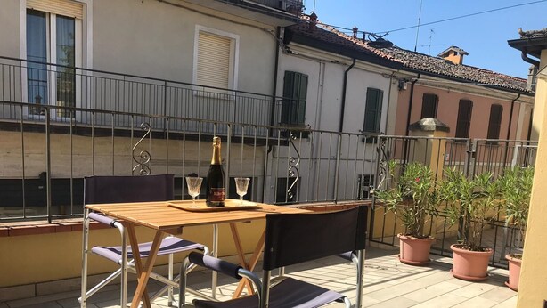 Un balcón con mesa de madera, dos sillas, una botella de champán y dos copas.