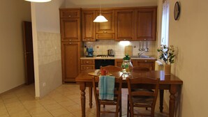 Una cocina con armarios de madera, una mesa de comedor con sillas, una cafetera y un reloj en la pared.