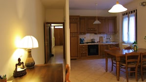 Una cocina con armarios de madera, una mesa de comedor y sillas. Hay una lámpara sobre la mesa y una ventana con cortinas.