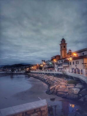 A coastal town with a prominent church tower, a stone bridge, and a beach. - The cardinal's house (Santo Stefano al Mare)