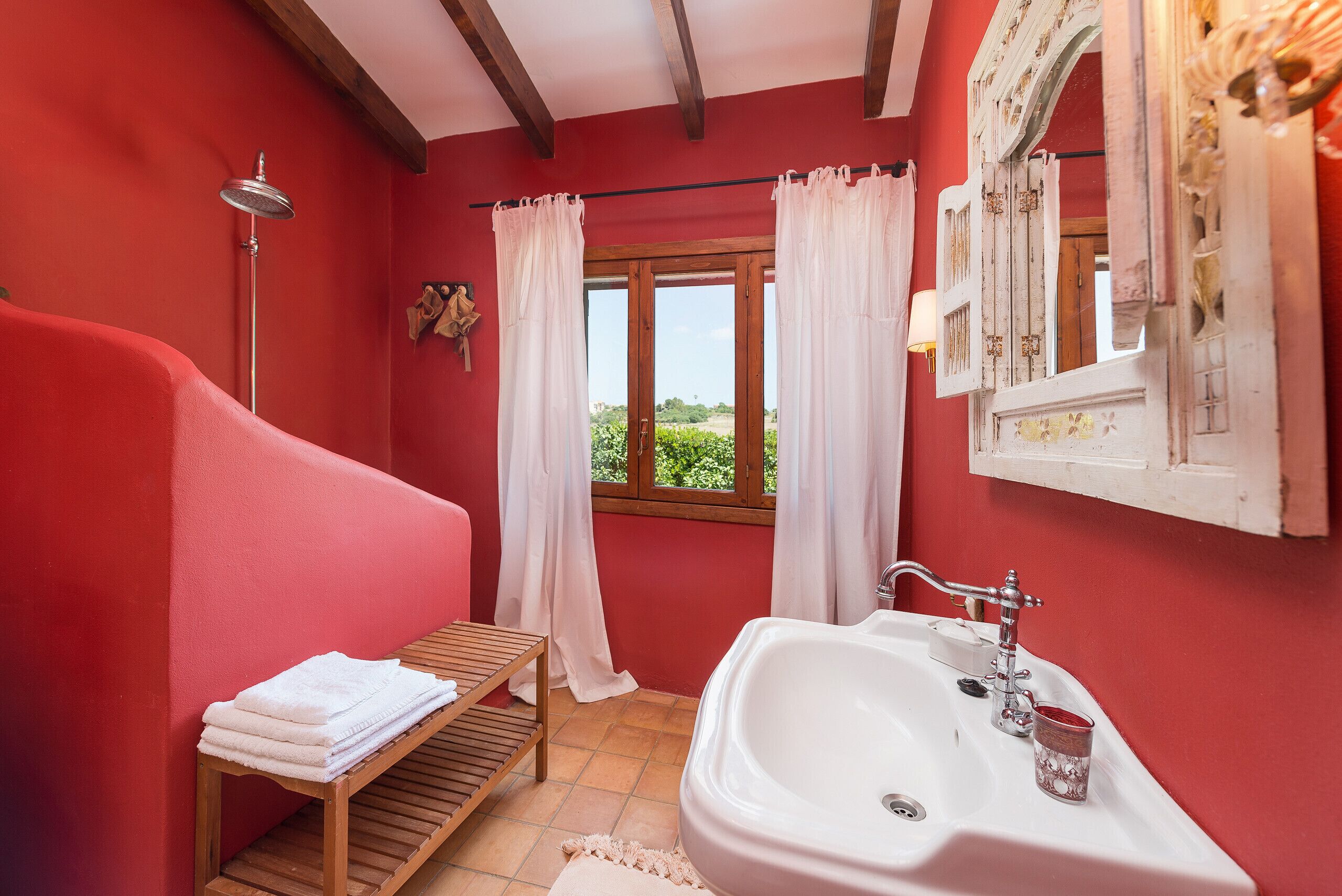 A bathroom with a wooden bench, a white sink, and a window with curtains.