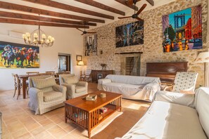 Un salon spacieux avec un plafond haut, des poutres apparentes, un mur en pierre et une cheminée. On y trouve plusieurs meubles, notamment un canapé, des fauteuils et une table basse.