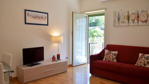 A living room with a TV, a glass table, a red sofa, and a sliding glass door to the outside.