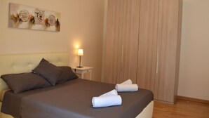 A neatly made bed with brown bedding and two white towels, a bedside lamp, and a wooden wardrobe.