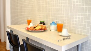 A breakfast table with a plate of toast, a glass of orange juice, a glass of milk, and a small container of sugar.