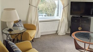 A living room with a sofa, a glass coffee table, a television, and a window with curtains. - Coastal City Coach House on Plymouth's historic hoe (Plymouth)
