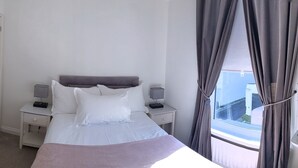 A neatly arranged bedroom with a bed, bedside tables, a dresser, and a window with curtains. - Coastal City Coach House on Plymouth's historic hoe (Plymouth)