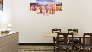 A dining area with a table and chairs, a wall-mounted artwork, a lamp, and a small plant on the table.