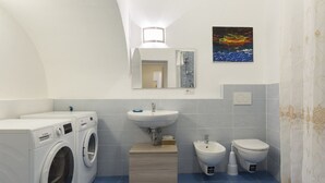 A compact bathroom with a washing machine, a sink, a bidet, and a toilet.