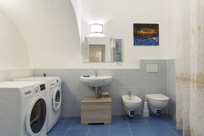 Une petite salle de bain équipée d’un lave-linge, d’un lavabo, d’un bidet et de toilettes.