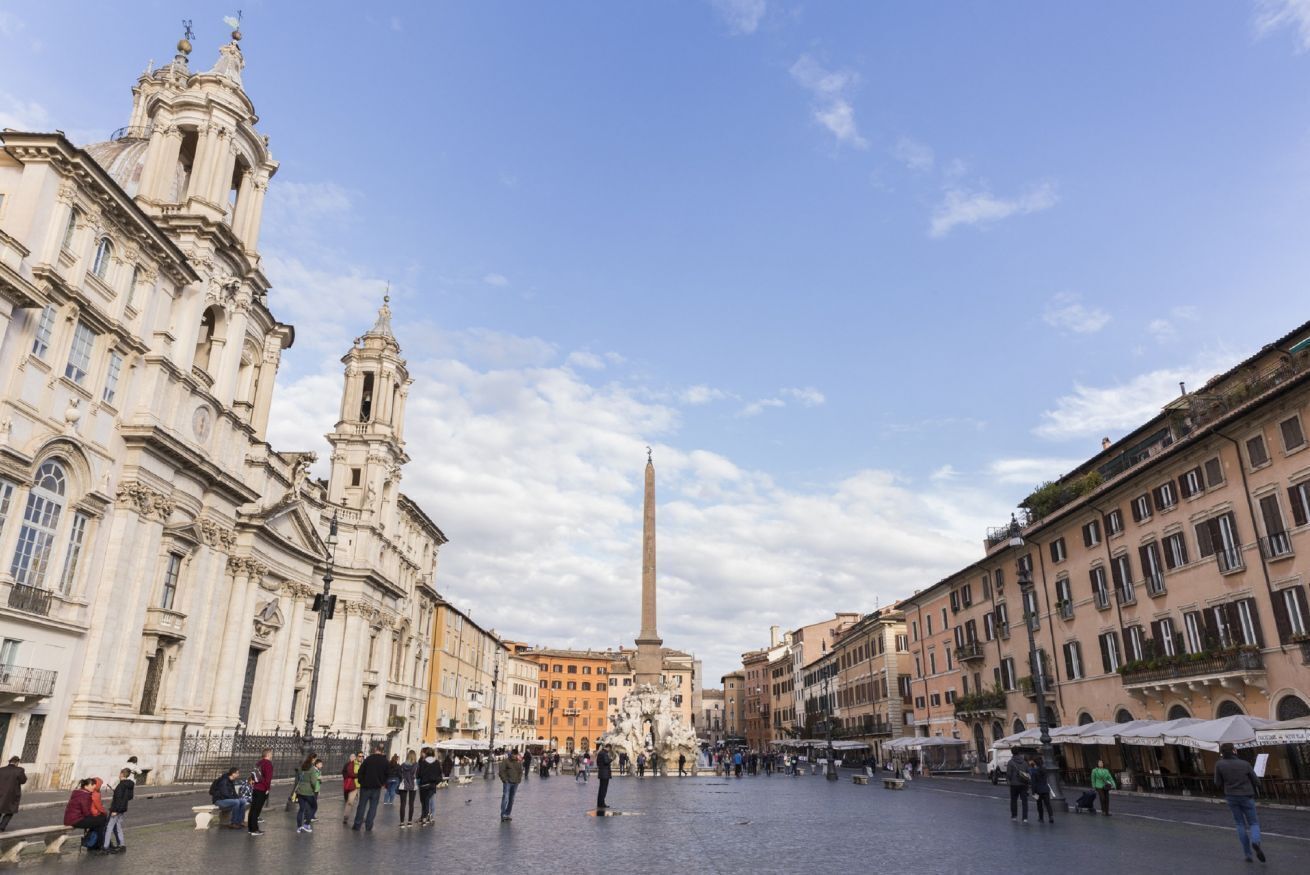 A historic square with a prominent obelisk and classical architecture.
