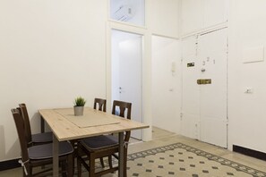 A room with a wooden table and four chairs, a potted plant, and a patterned rug. There is a white door with a number plate and a phone on the wall. - Stay in Rome Apartments Central Navona Sq (Roma)
