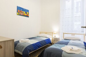 A bedroom with two single beds, a wooden nightstand, a small desk, and a wall-mounted painting of tulips. - Stay in Rome Apartments Central Navona Sq (Roma)