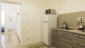 A compact kitchen with a refrigerator, microwave, kettle, and coffee maker on the counter.