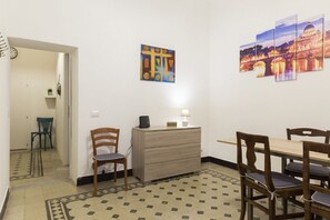 A room with a dining table, chairs, a desk with a lamp, a chair, a wall clock, and a painting of a bridge. - Stay in Rome Apartments Central Navona Sq (Roma)