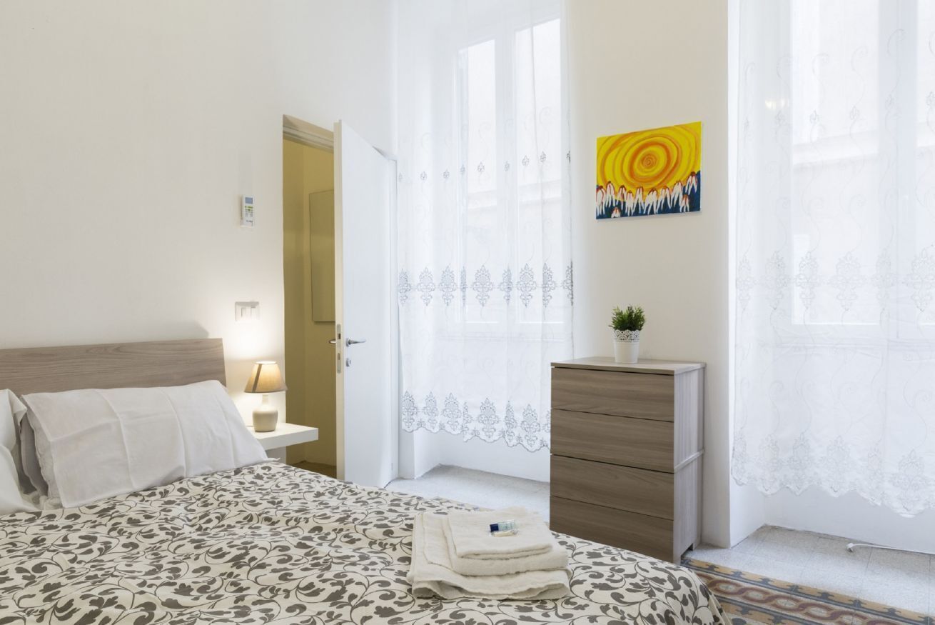 A bedroom with a bed, bedside table, lamp, dresser, and a window with curtains.