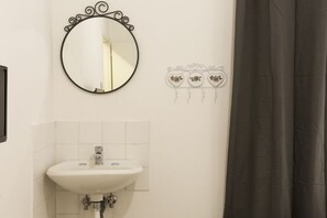 Een badkamer met een witte wastafel, een ronde spiegel met decoratieve lijst, en een wandlamp met bloemenmotief.