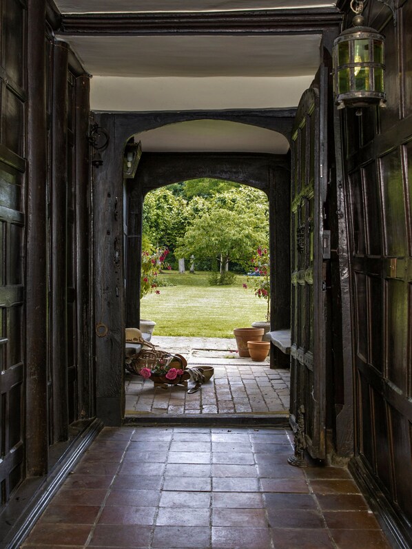 An open doorway leading to a garden with a lawn, potted plants, and a wicker basket on the floor.