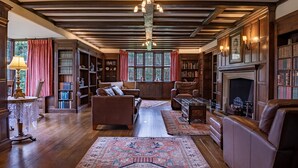 A library with wooden bookshelves, leather sofas, and a fireplace.