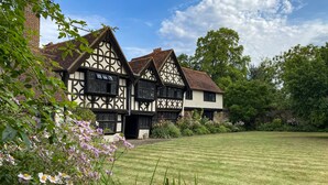 A traditional Tudor-style building with a symmetrical facade, multiple chimneys, and a well-maintained lawn in front.