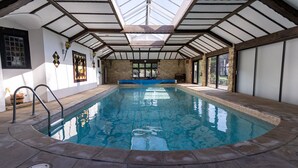 An indoor swimming pool with a high ceiling, stone walls, and large windows.
