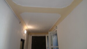 Um quarto com teto branco, luminária e porta semiaberta dando para um cômodo escuro.