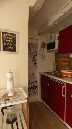 A kitchen with a microwave, red cabinets, a wooden floor, and a chalkboard with writing.